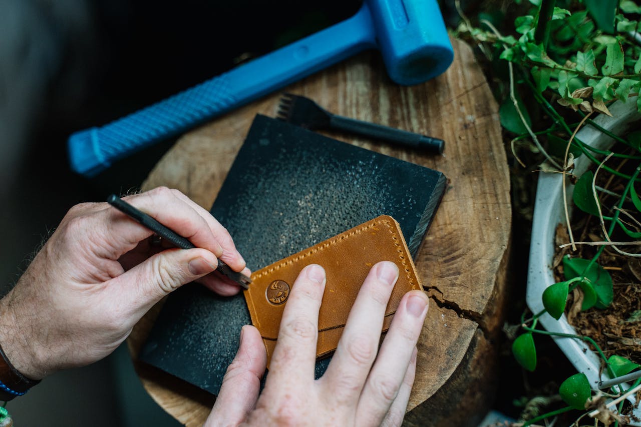 Hands crafting a leather wallet on a tree stump with tools outdoors. A creative and artisanal approach to leatherwork.